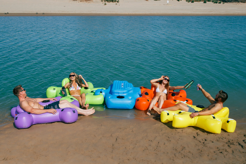 4 people in bathing suite floating in Red, Green, Purple and Yellow Fluzzle Tubes puzzle shaped inflatable and interlocking river, lake or pool tube with inflatable back rest, mesh bottom, expandable cup holders, 2 durable handles. 12 nylon connectors. Interlocking floating cooler. 